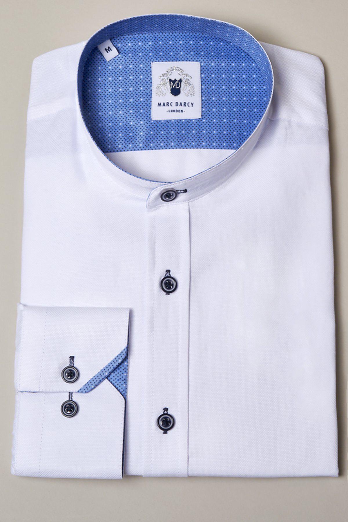 The ARCHIE White Grandad Collar Shirt by Marc Darcy features navy buttons and a stylish design, displayed neatly folded on a plain light surface with the brand label inside the collar.