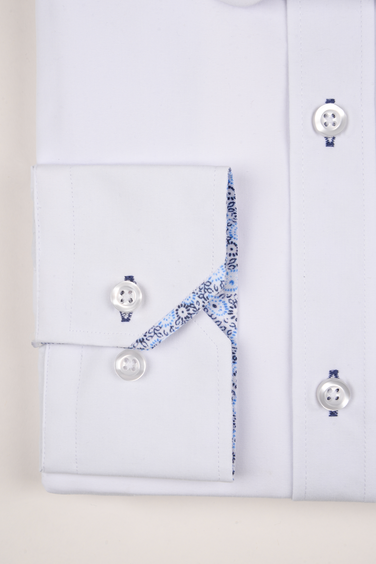 A close-up of the marcdarcy BENSON White Penny Collar Shirt With Collar Bar shows its white buttons, blue stitching, and a folded cuff revealing a blue and white patterned lining—ideal for formal occasions.