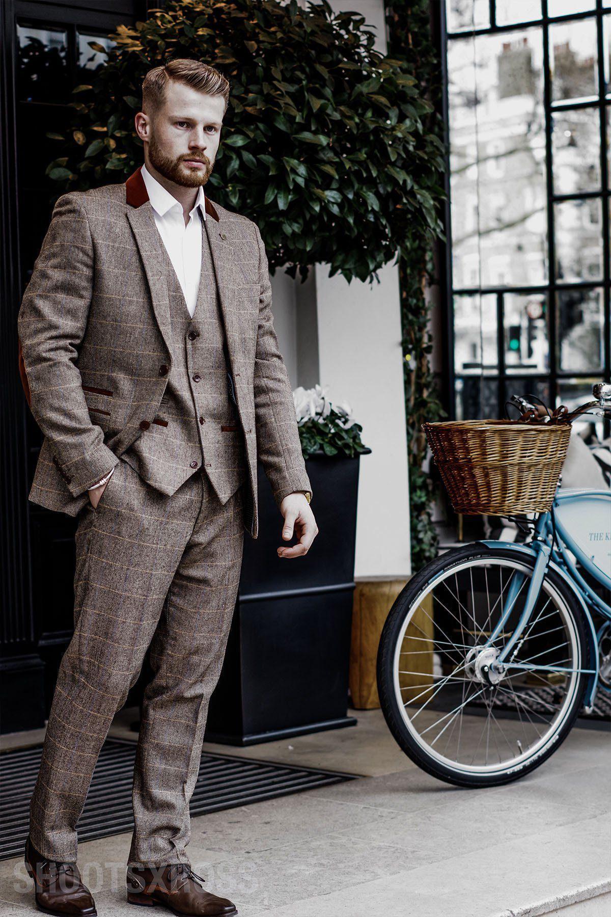 A man with a short beard wears the marcdarcy Blogger Style | DX7 Suit as worn by Jonny Hammond, featuring a velvet contrast collar, and stands outside by a blue bicycle near large windows and green foliage.