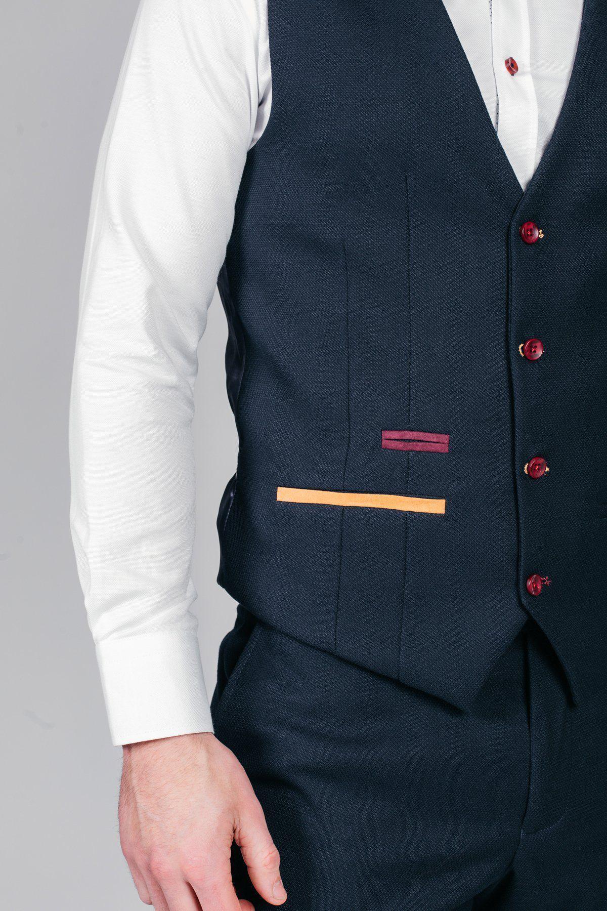 Nick Pope, goalkeeper for Newcastle United and England, wears the marcdarcy JD4 Navy Suit featuring a dark blue vest and pants with red buttons, maroon and orange pocket accents, over a white shirt. Only the torso and one arm are visible against a plain background.
