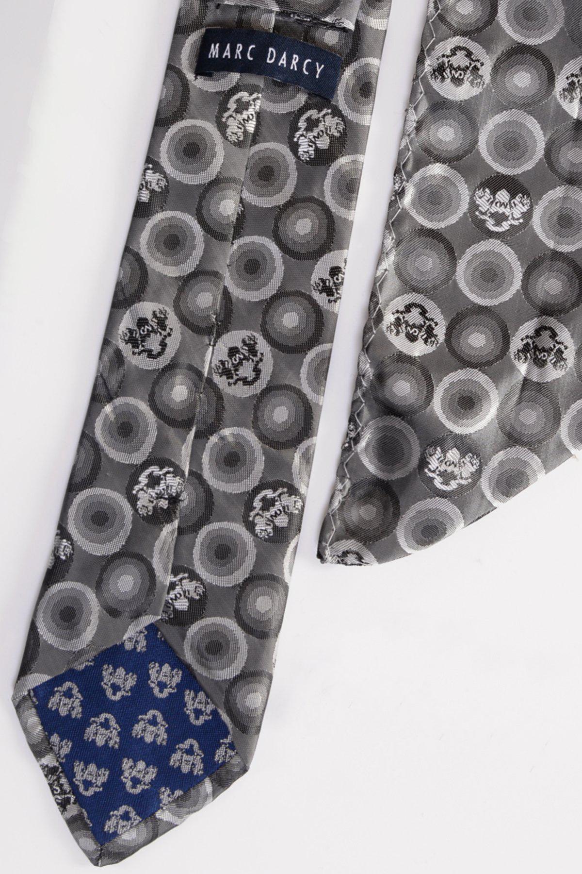 The BUBBLES Grey Bubble Circle Print Tie and Pocket Square Set by Marc Darcy features a gray tie with circular designs, a blue tip with white patterns, and a sewn brand label at the back for a sophisticated formal touch.
