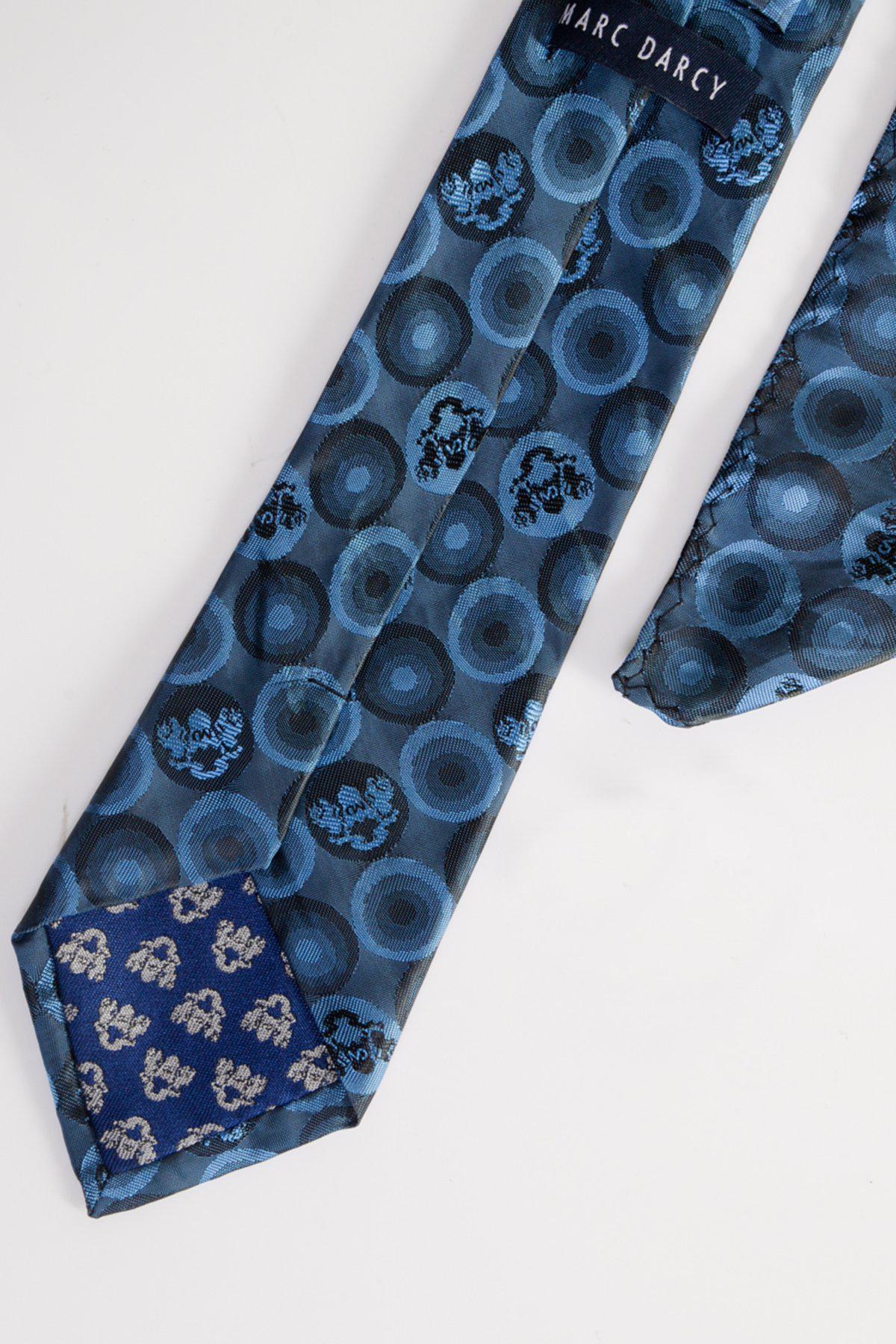 The BUBBLES - Sky Teal Bubble Circle Print Tie and Pocket Square Set by Marc Darcy features bold circular designs in blue tones, with a branded label near the top. The tie is displayed on a white background.