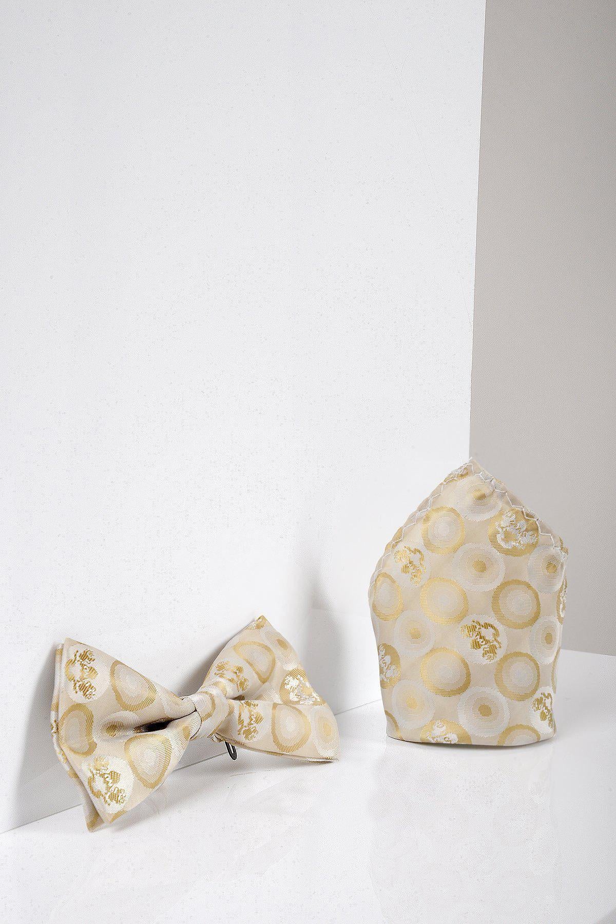 The Marc Darcy BUBBLES - Stone Bubble Circle Print Bow Tie and Pocket Square Set, featuring a light gold circular pattern and adjustable strap, is displayed on a white reflective surface with a white and beige background.