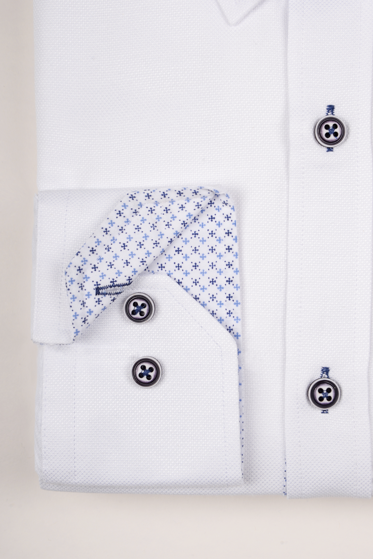 The CHARLIE by Marc Darcy is a white Oxford shirt with blue buttons, made from a textured cotton blend and featuring an inside cuff lining with a subtle blue geometric pattern.
