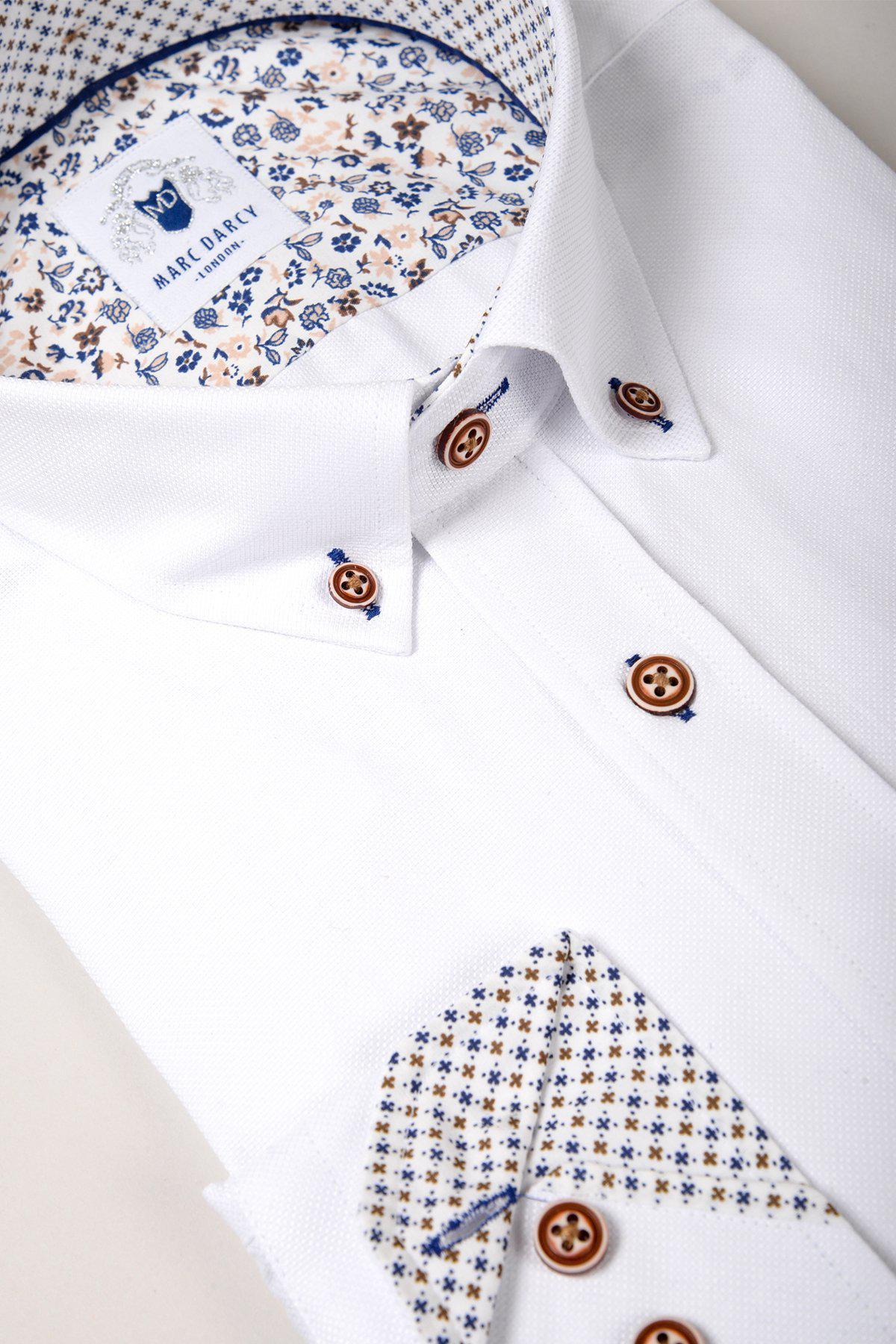 The CHARLIE White Oxford Shirt by Marc Darcy features soft cotton blend fabric, tan buttons, blue stitching, and a patterned blue and tan inner collar and cuffs. The Marc Darcy label is visible inside the collar.