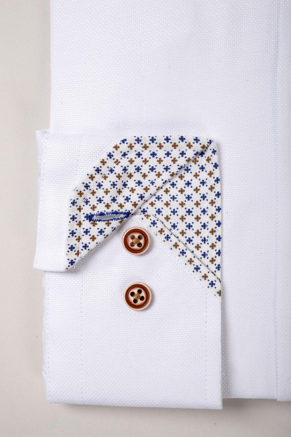 A close-up of the CHARLIE White Oxford Shirt by Marc Darcy shows its cotton-blend cuff with two tan contrast buttons and a folded corner revealing a patterned inner lining with small blue and brown floral motifs.