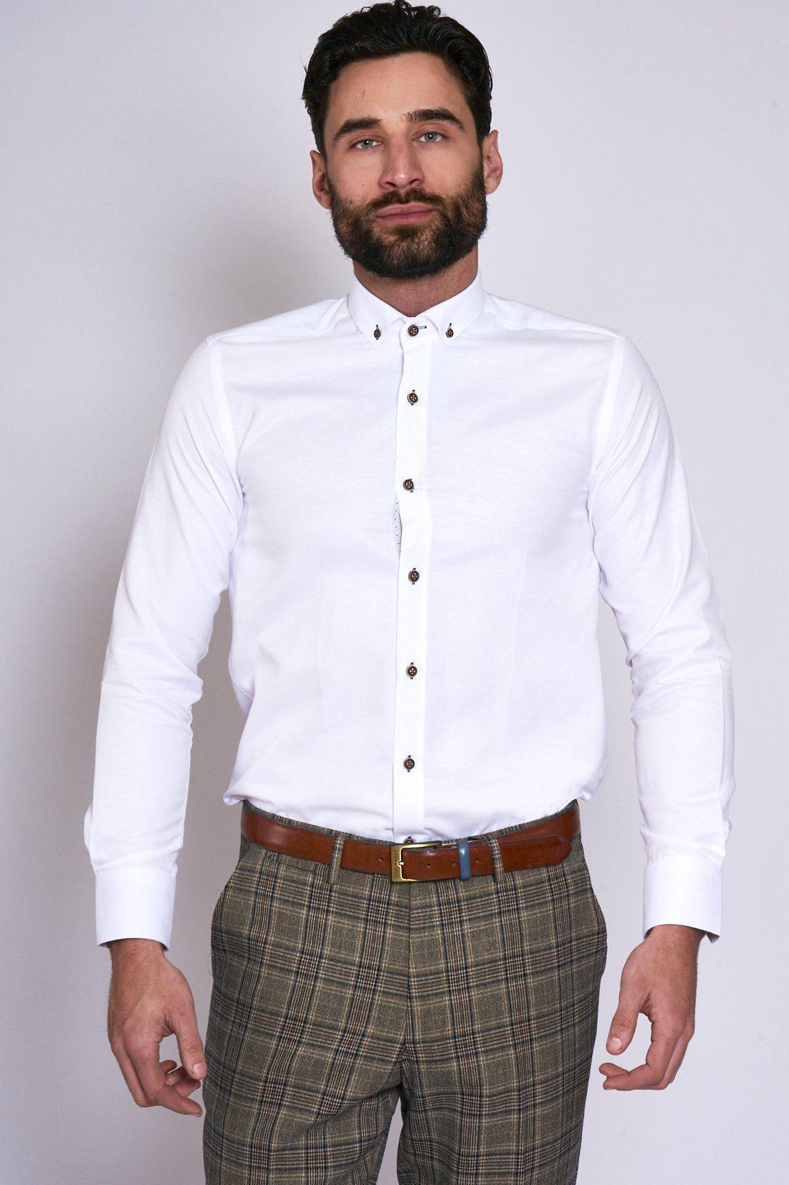 A man wears the Marc Darcy CHARLIE White Oxford Shirt with tan buttons and brown plaid trousers, paired with a brown belt, standing against a plain light background.
