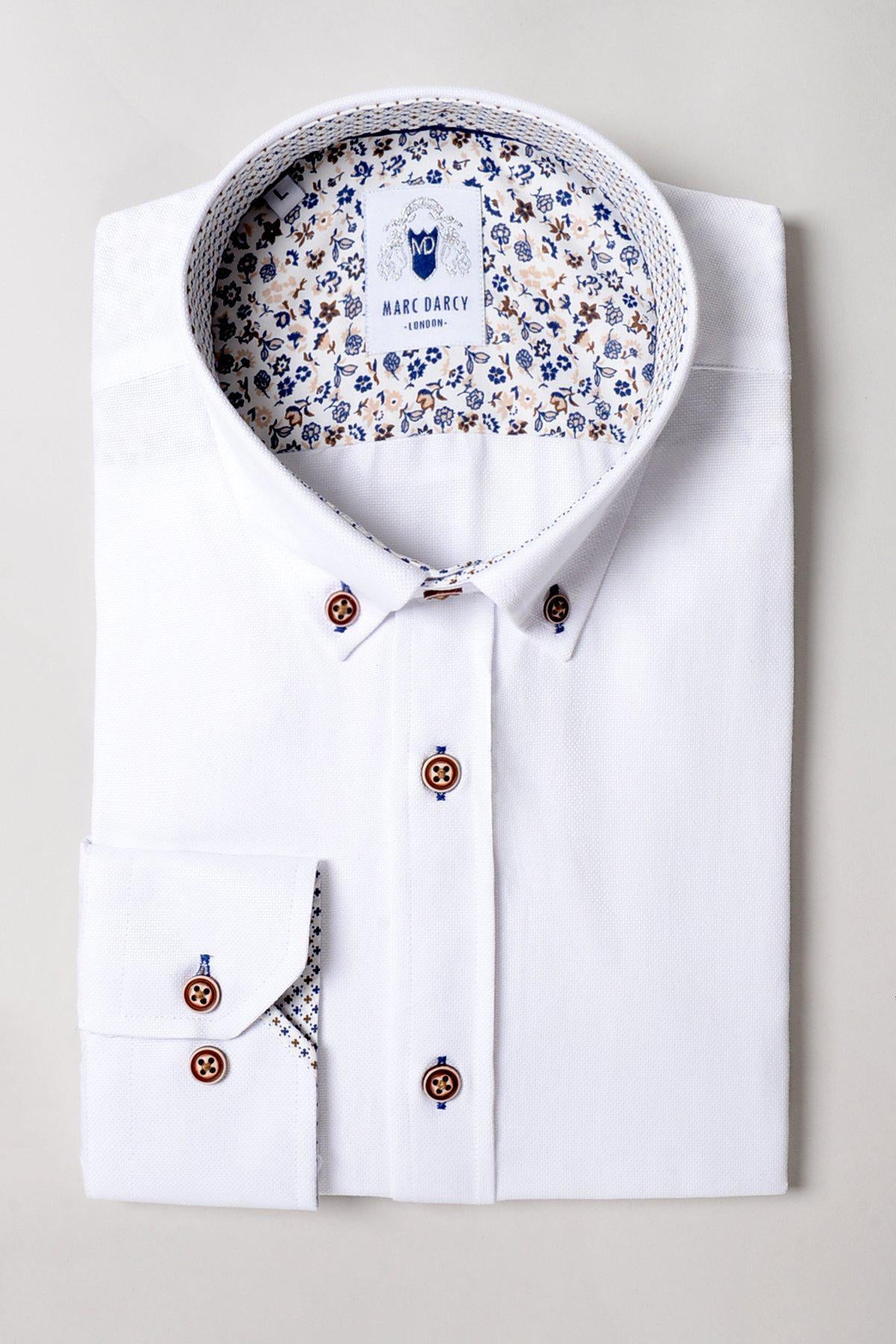 The Marc Darcy CHARLIE White Oxford Shirt features tan buttons and a floral pattern on the inner collar and cuffs, shown neatly folded against a light background.