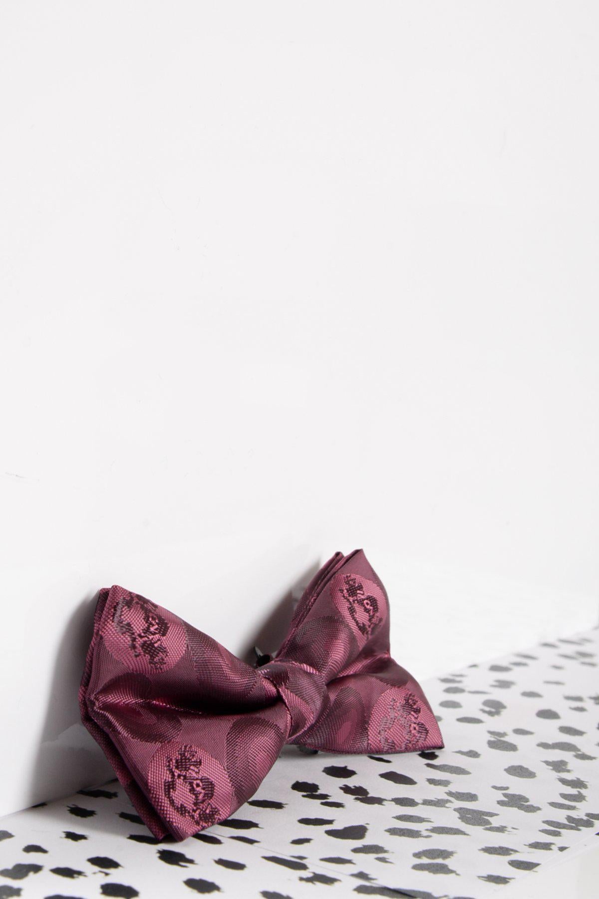 The Marc Darcy Children's Berry Bubble Circle Print Bow Tie, featuring a playful pattern and adjustable neck strap, is displayed against a white wall on a black and white spotted surface.