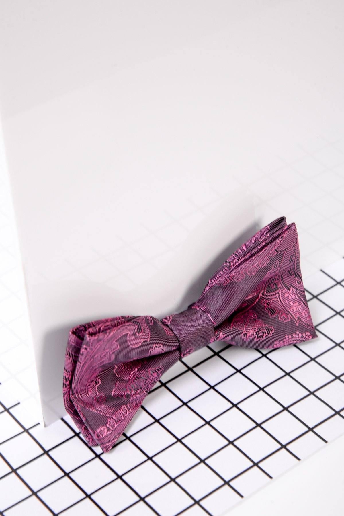 The Marc Darcy Childrens Berry Paisley Print Bow Tie is shown on a white panel with a black grid underneath. This stylish accessory offers an adjustable neck strap for the perfect fit.