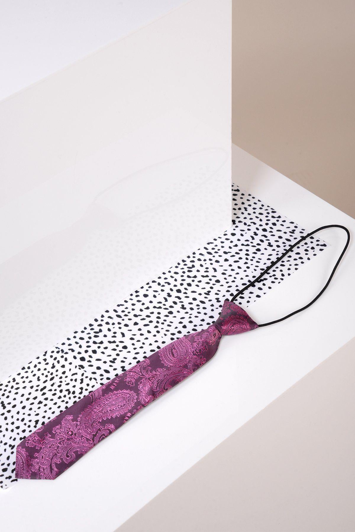 The Marc Darcy Childrens Berry Paisley Print Tie, featuring an adjustable elasticated neck strap, is displayed on a white surface with black dots, set against a minimal beige and white geometric background.