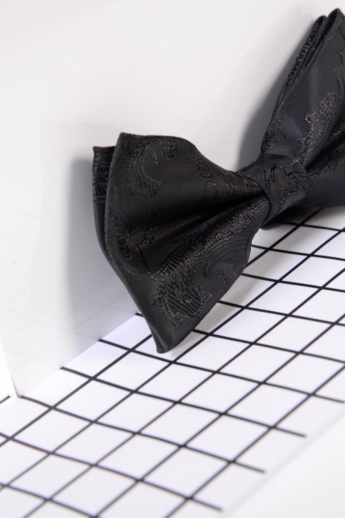 A close-up of the Marc Darcy Children's Black Paisley Print Bow Tie on a white surface with a black grid pattern, offering a modern, stylish backdrop for this formal accessory.