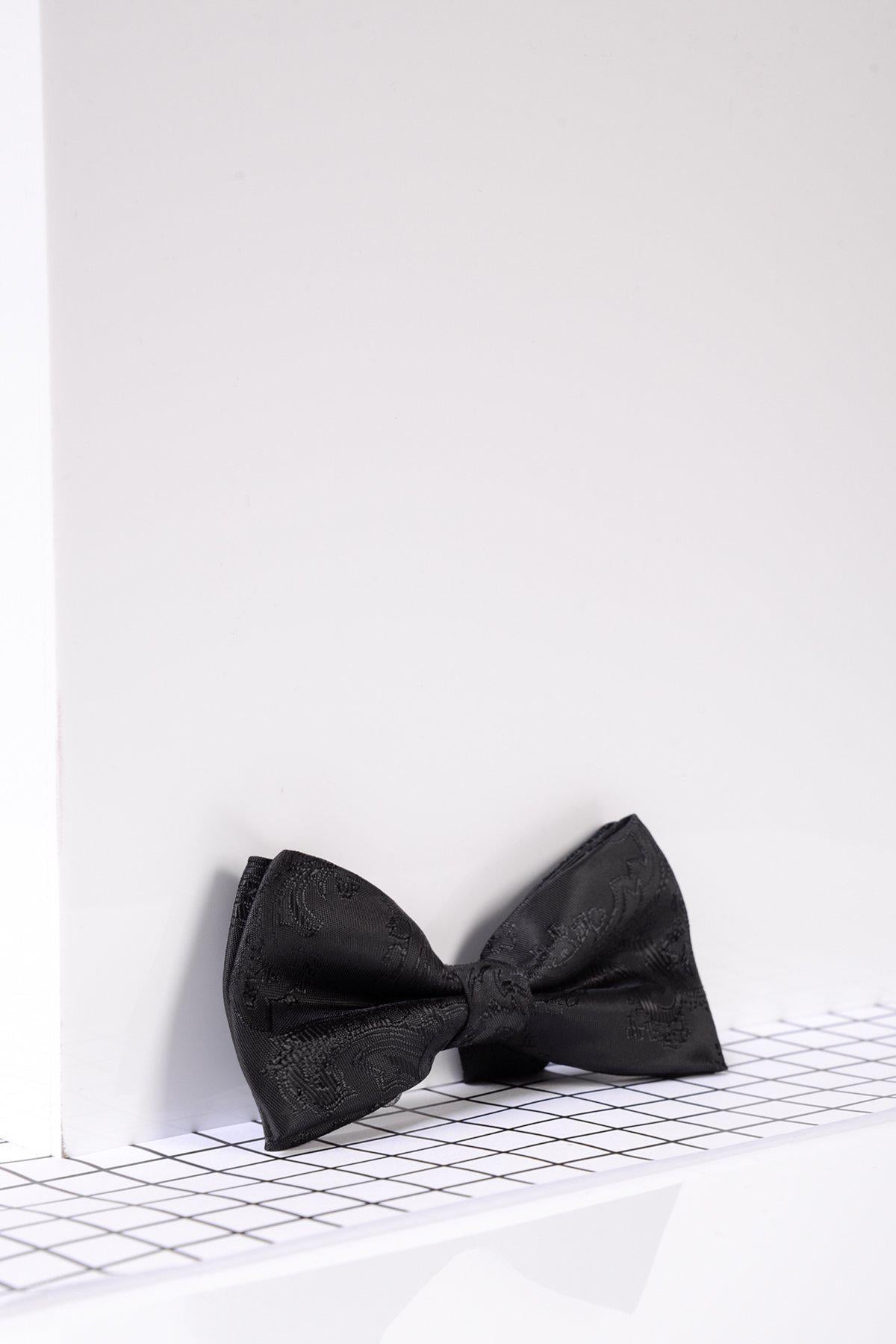 The Marc Darcy Children's Black Paisley Print Bow Tie, featuring a subtle pattern, is displayed on a white surface with a black grid—ideal for adding charm to kids' suits and formal outfits.