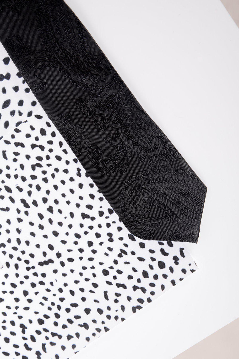 The Marc Darcy Children's Black Paisley Print Tie, pre-tied and silky, is displayed diagonally on white fabric with black polka dots.