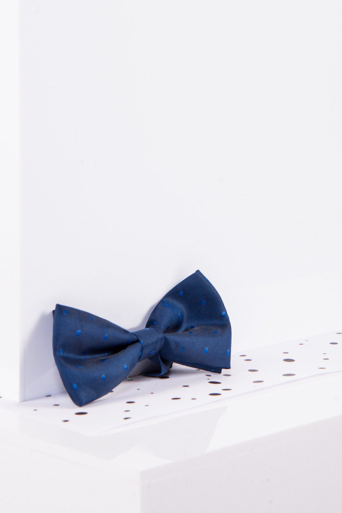 The Marc Darcy Children's Blue Polka Dot Bow Tie, featuring an adjustable neck strap, is displayed on a white surface with black speckles.