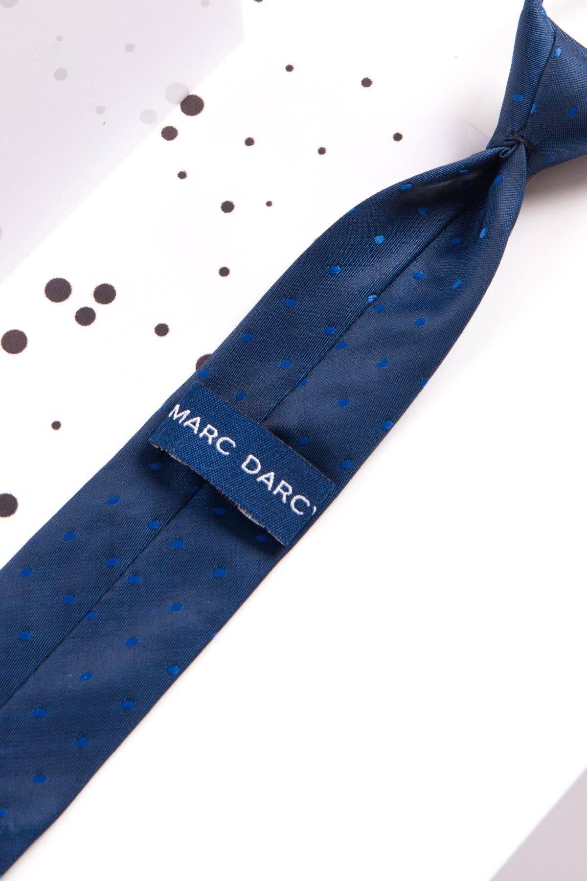 The Childrens Blue Polka Dot Print Tie by Marc Darcy features small blue dots and an adjustable elasticated neck strap for easy wear. The pre-tied navy blue tie is displayed on a white surface with black dots.