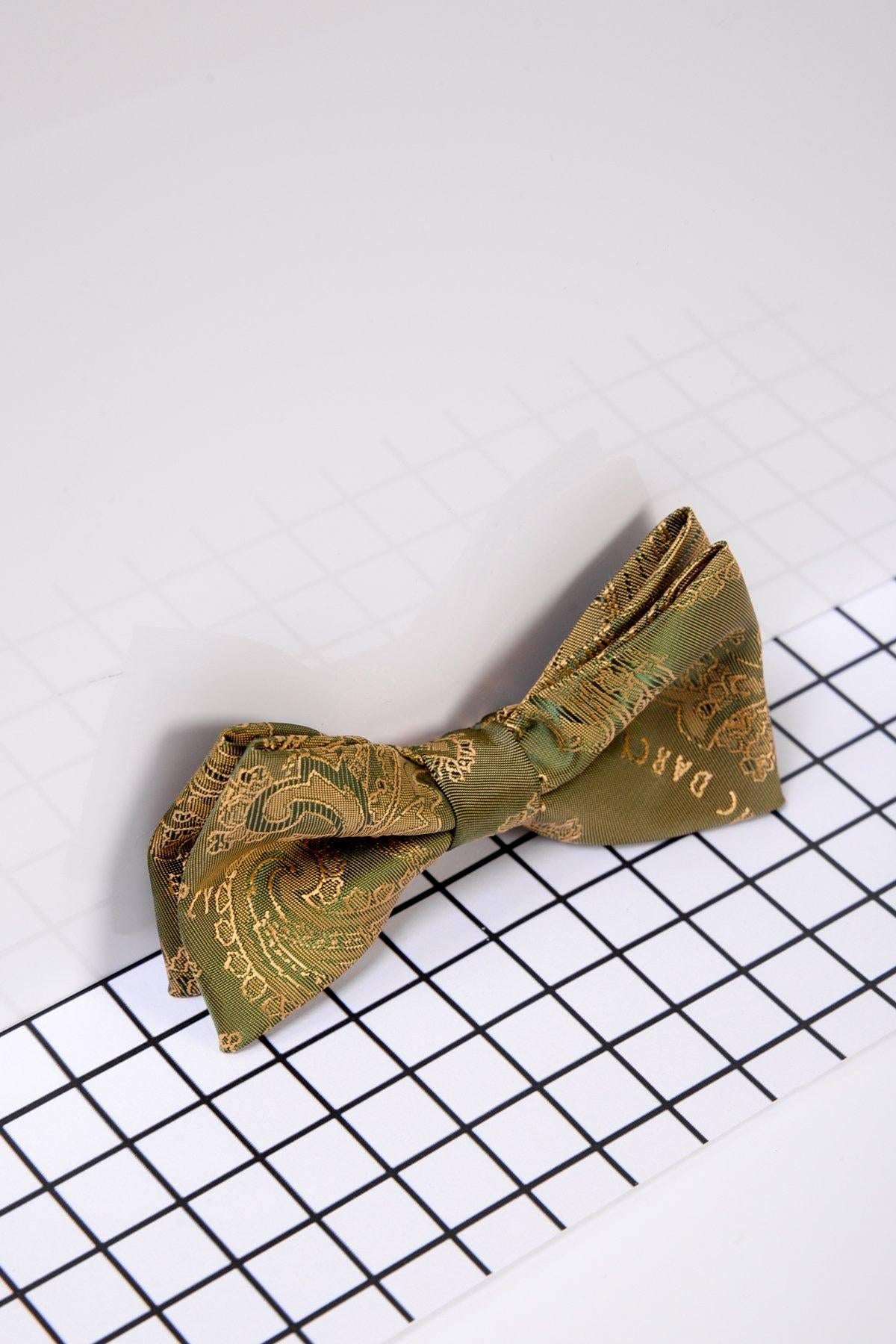 The Marc Darcy Childrens Gold Tan Paisley Print Bow Tie features elegant gold patterns, adding stylish flair, and is displayed on a grid-patterned surface with a white and light gray background.