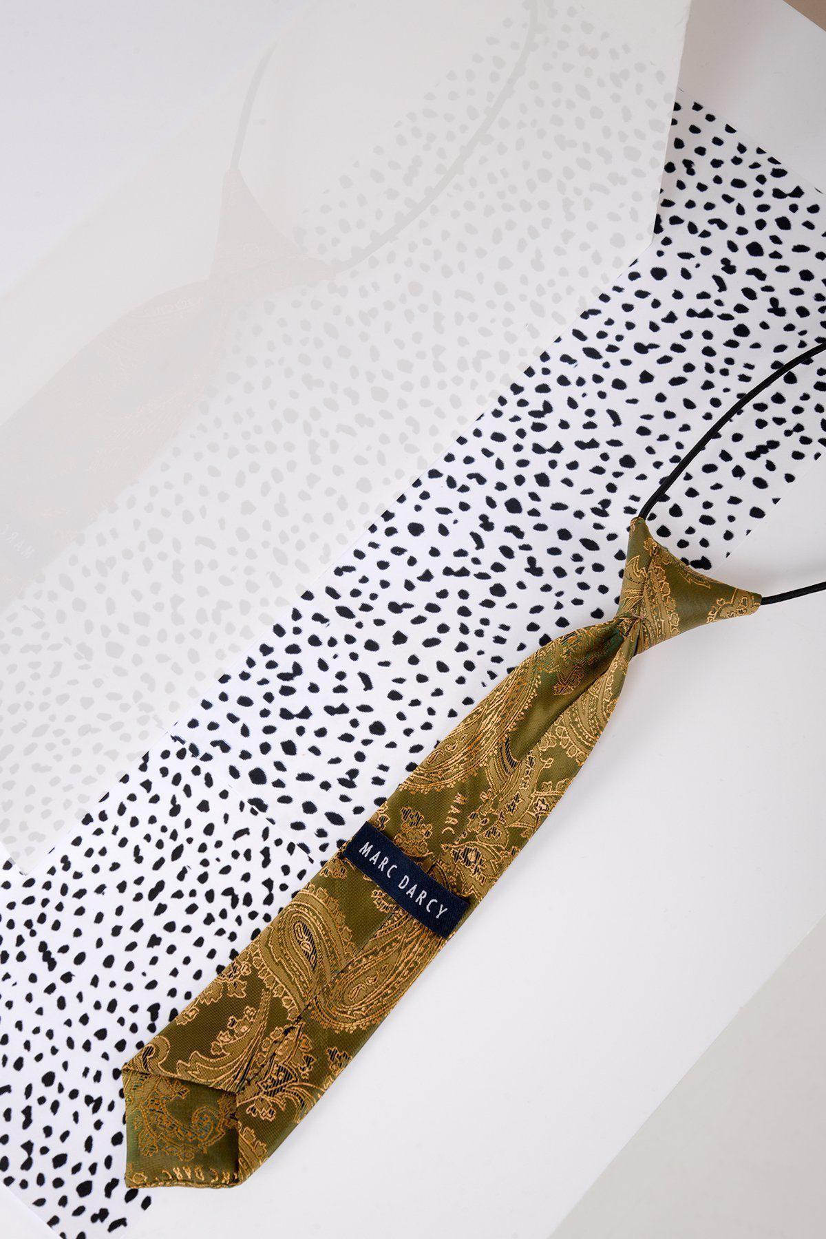 The Marc Darcy Childrens Gold Tan Paisley Print Tie, featuring a silky pre-tied design and adjustable elasticated neck strap, rests on a white surface with black dots, its reflection shimmering on the glossy finish.