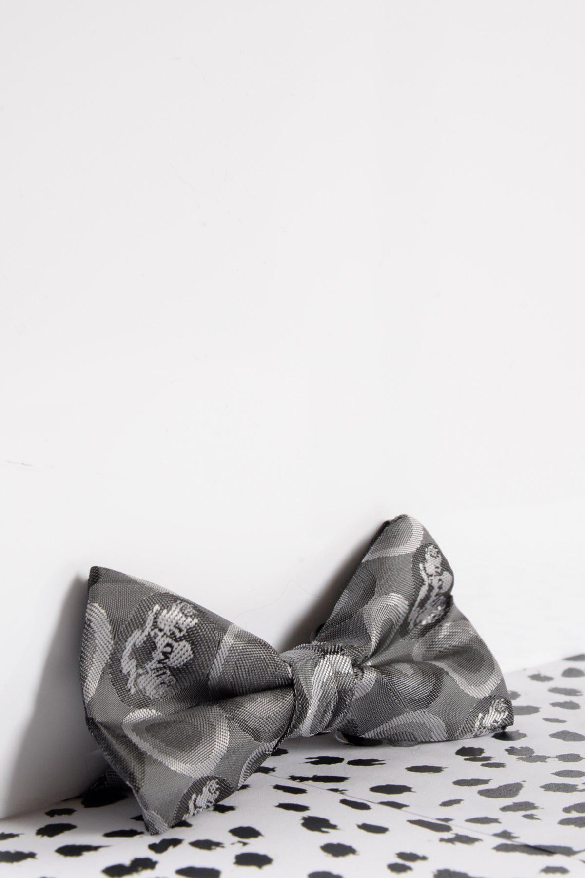 The Marc Darcy Childrens Grey Bubble Circle Print Bow Tie, featuring an adjustable strap, sits on a white surface with black spots—an adorable accessory for kids.