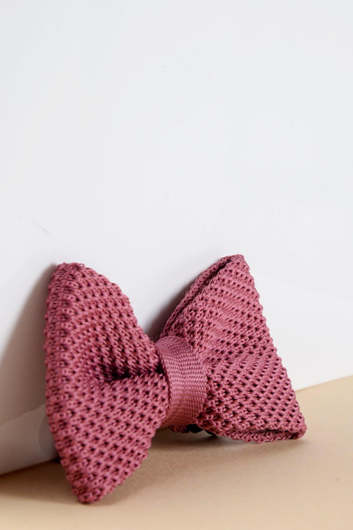 The Children's Knitted Bow Tie in Berry by Marc Darcy features a textured pink knit and adjustable neck strap, shown against a white and beige background—a charming formal accessory for boys.