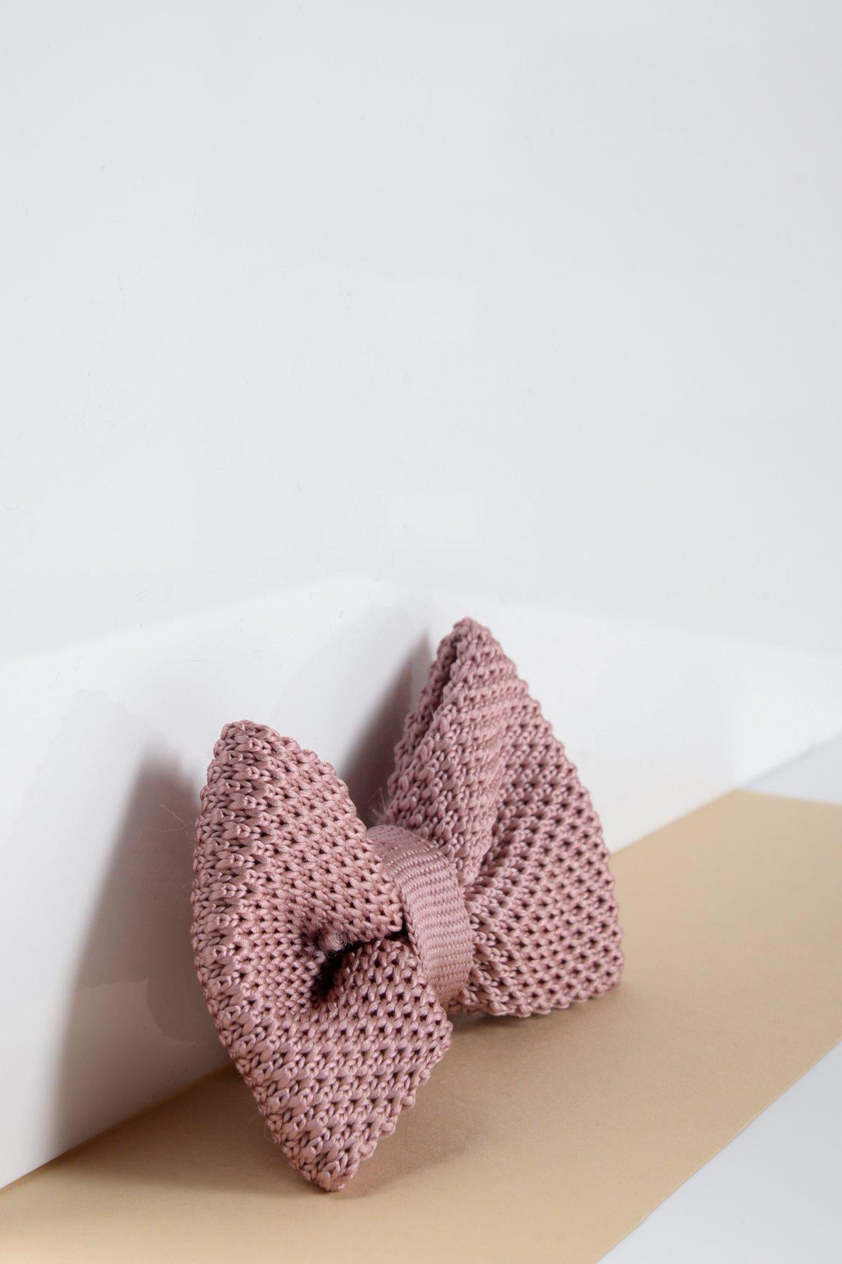 The Marc Darcy Children's Knitted Bow Tie in Blush Pink features a textured weave and comes pre-tied for easy wear, shown prominently against a white and beige background.