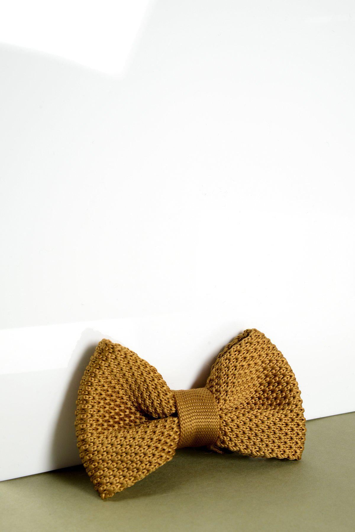 The Marc Darcy Children's Knitted Bow Tie in Gold sits on a light green surface with a white background.