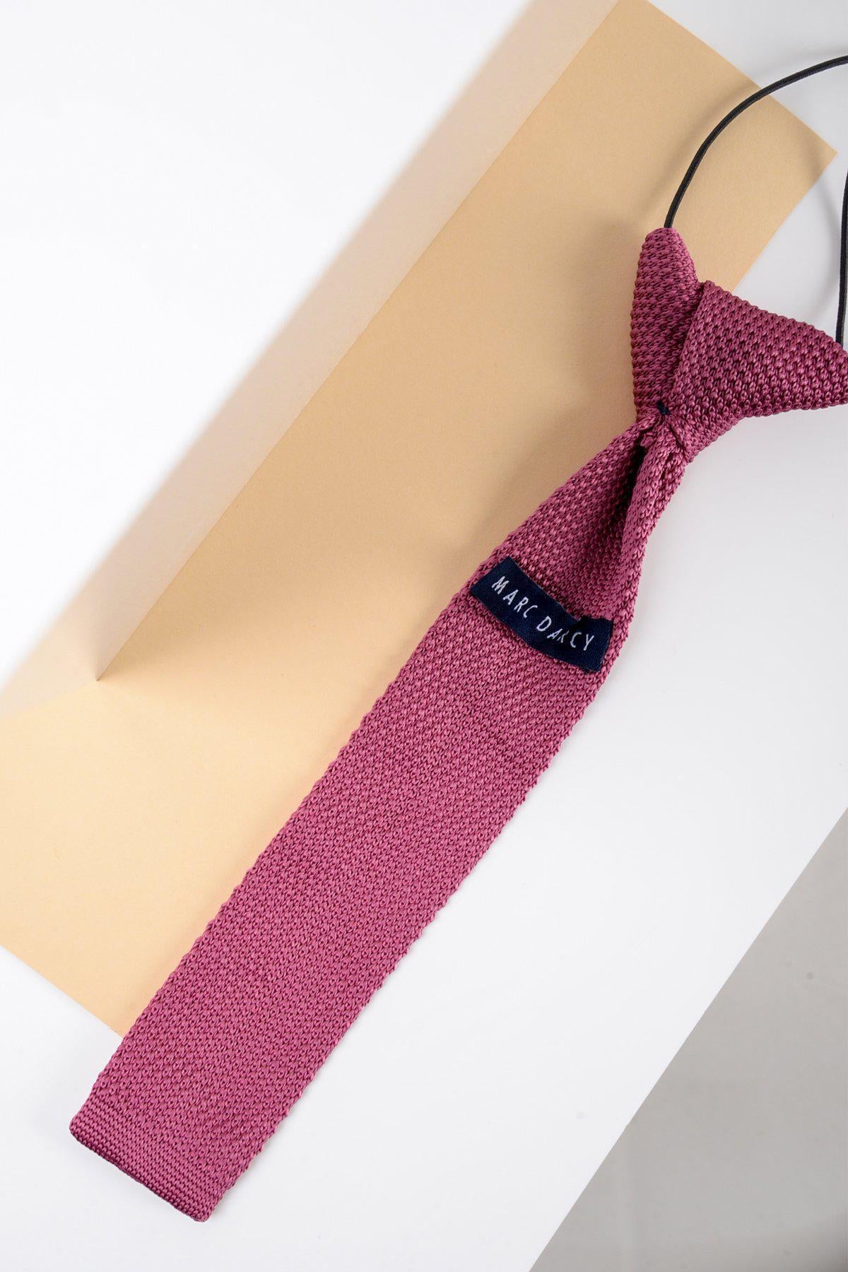 A Marc Darcy Children's Knitted Tie in Berry is displayed on a flat surface, partially covering a beige envelope—an ideal formal accessory for boys on special occasions.