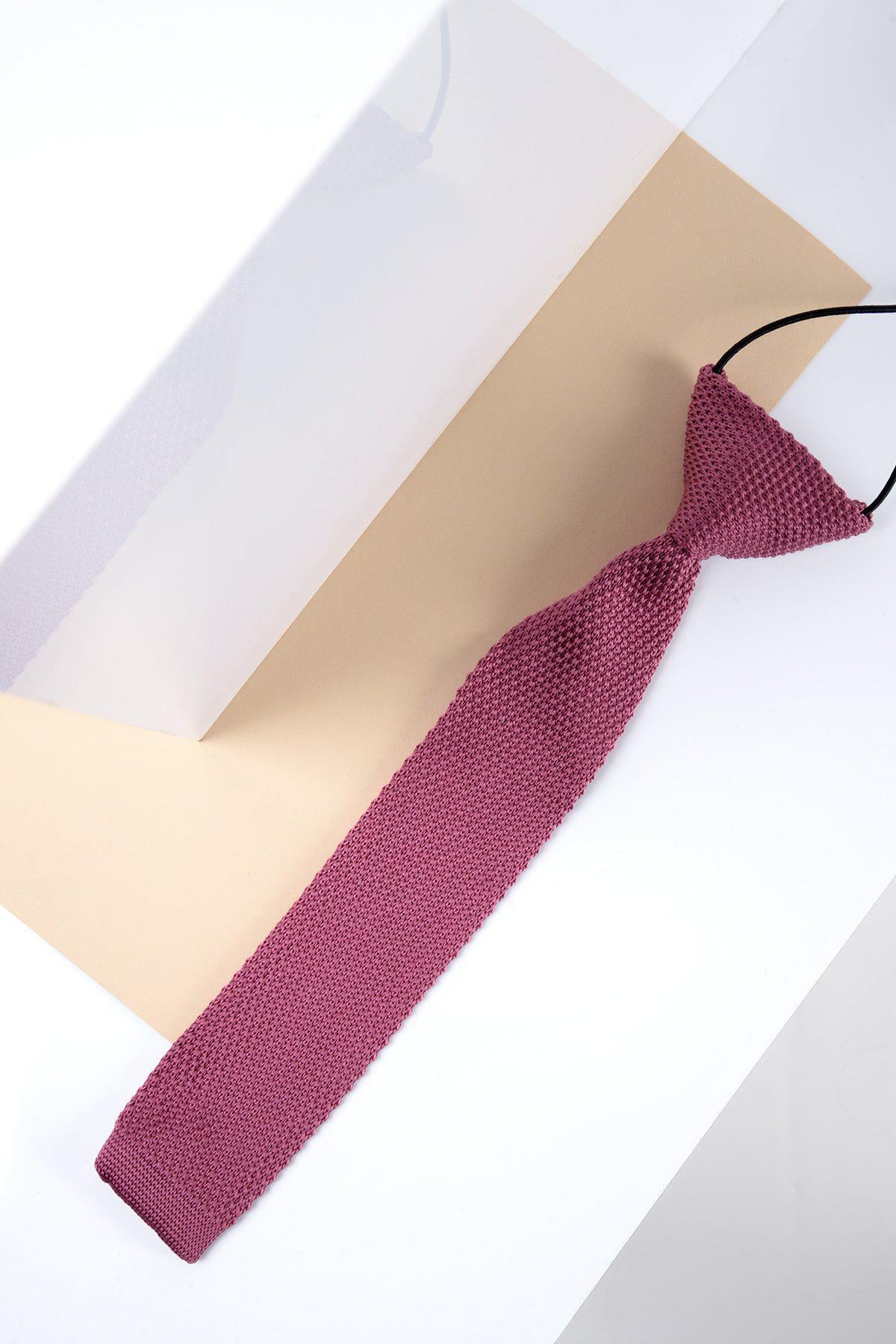 The Marc Darcy Childrens Knitted Tie in Berry, featuring a textured dark pink design and black adjustable neck strap, is displayed flat on a beige and white geometric background.