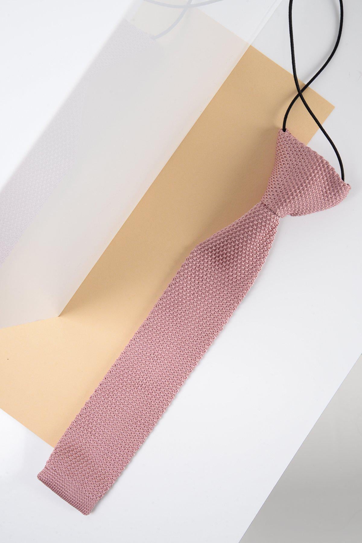 The Children's Knitted Tie in Blush Pink by Marc Darcy, featuring a black adjustable neck strap, is displayed on a beige and white geometric backdrop—an ideal accessory to add subtle charm to any formal occasion.