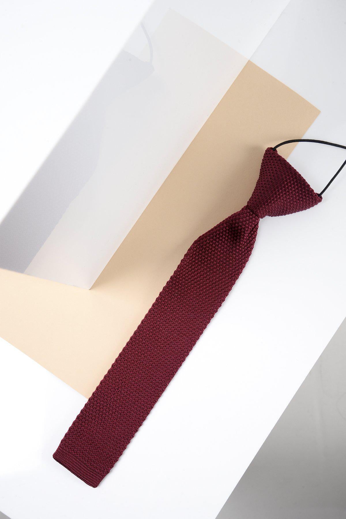 The Marc Darcy Childrens Knitted Tie in Wine, featuring an elastic band, is displayed on a white and beige geometric background—ideal for adding style to any formal occasion.