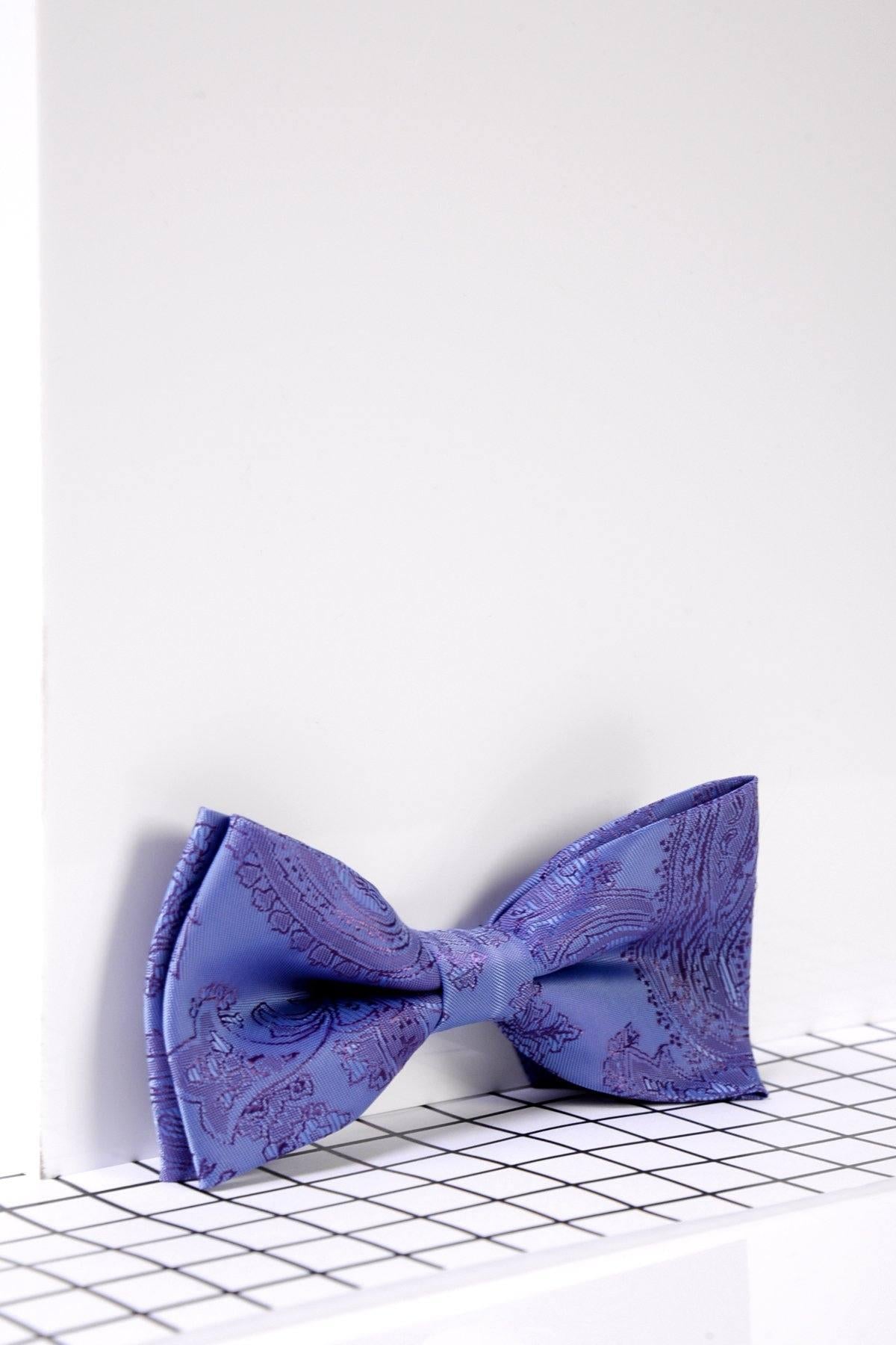 The Marc Darcy Children's Lilac Paisley Print Bow Tie, featuring an adjustable neck strap, is displayed on a modern black grid surface with a white wall backdrop—ideal for boys' formalwear.