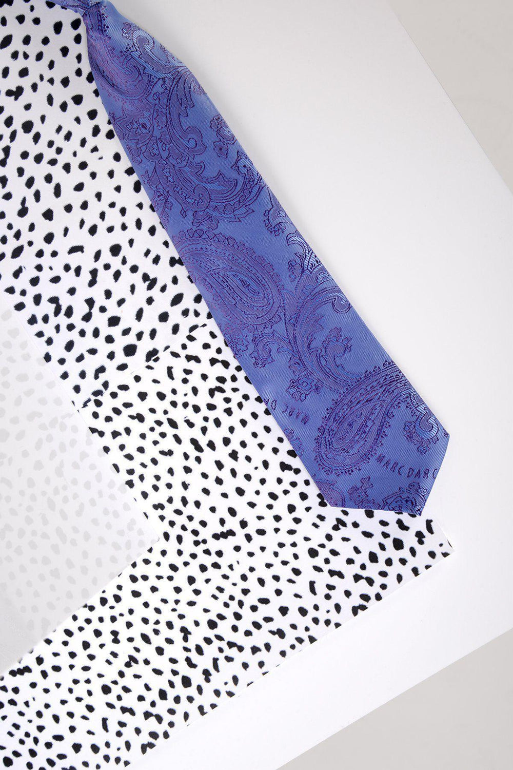 The Marc Darcy Children's Lilac Paisley Print Tie is shown diagonally on a white background with black irregular spots. It features an adjustable neck strap for comfort.
