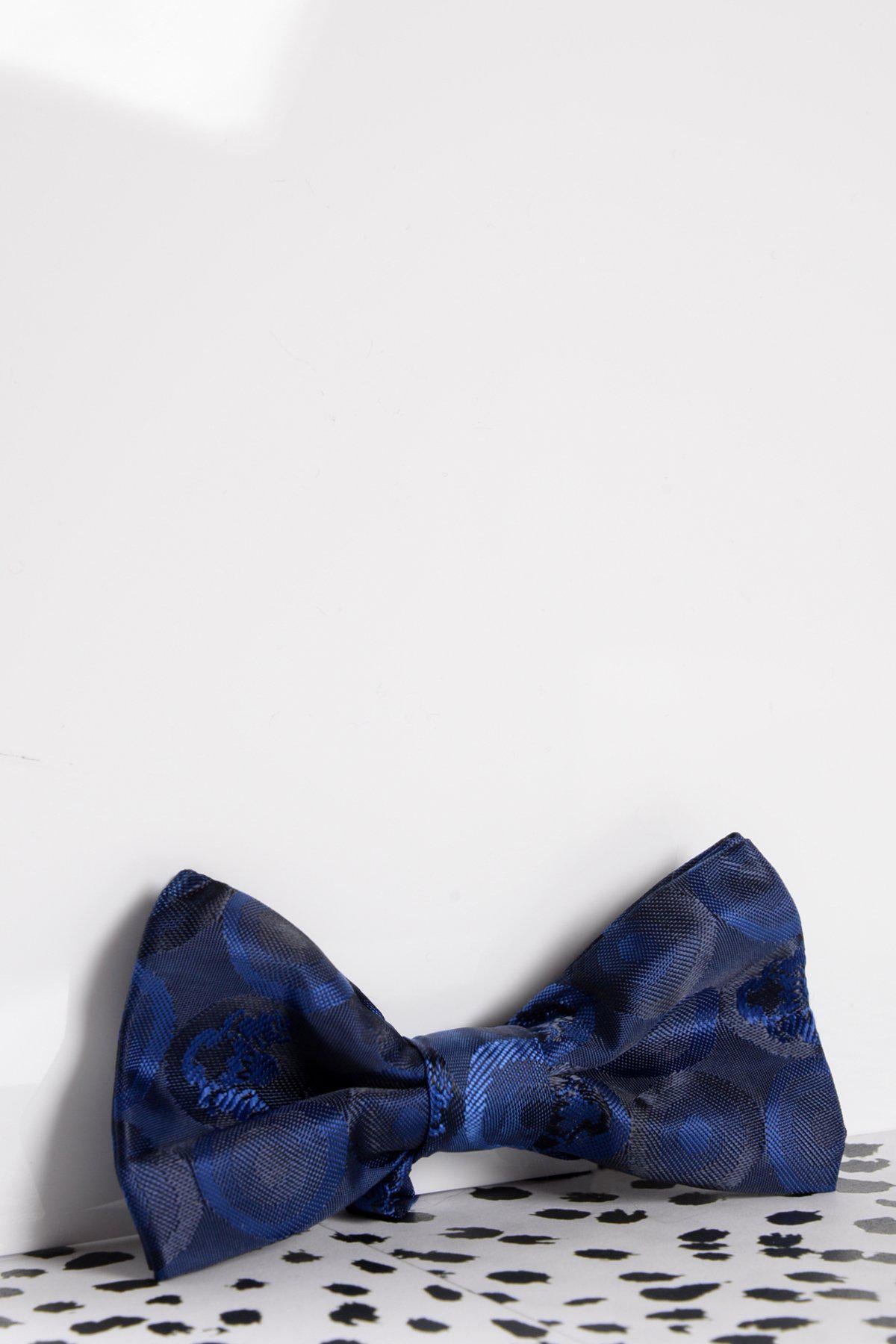 The Marc Darcy Children's Navy Bubble Circle Print Bow Tie, featuring an adjustable neck strap and blue pattern, is displayed on a white surface with a black speckled bottom and a plain white background.