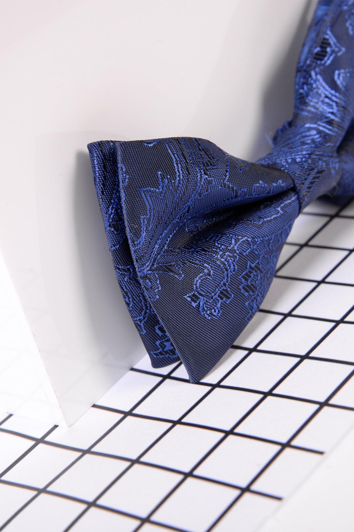 A close-up of the Marc Darcy Childrens Navy Paisley Print Bow Tie on a white grid-patterned surface, partially reflected in a mirror—ideal for formal looks and featuring an adjustable neck strap.