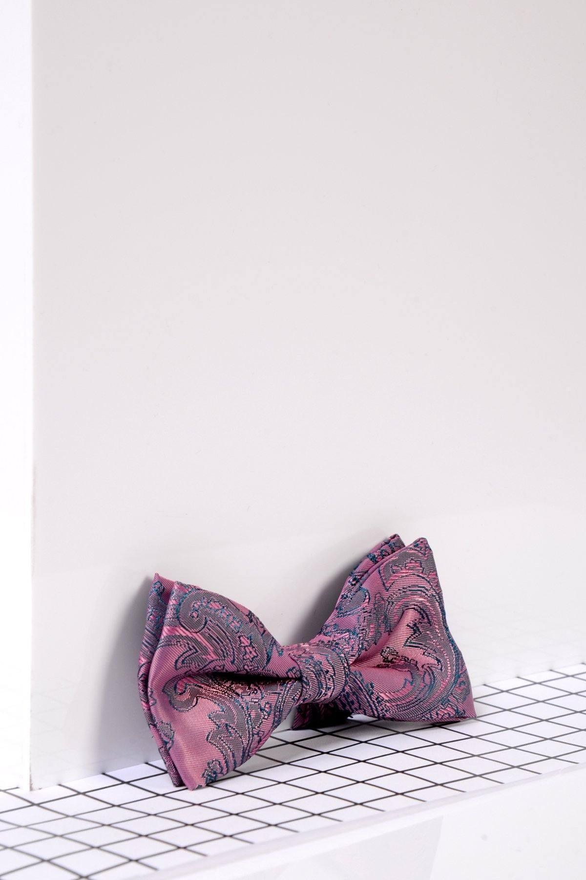 The Marc Darcy Children's Pink Paisley Print Bow Tie, ideal for boys' formal wear or page boy suits, is displayed on a white grid shelf with a blue and gray paisley pattern against a white background.