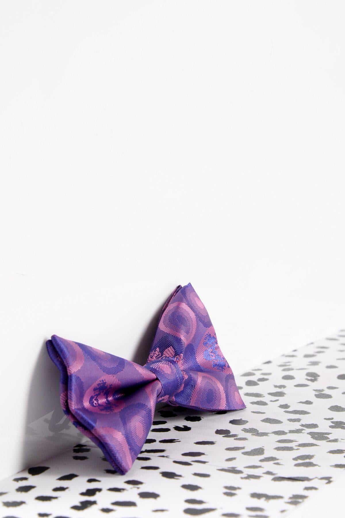 The Marc Darcy Children's Purple Bubble Circle Print Bow Tie features playful purple and pink patterns with an adjustable neck strap, styled on a white surface with black and white spots—ideal for boys' partywear.