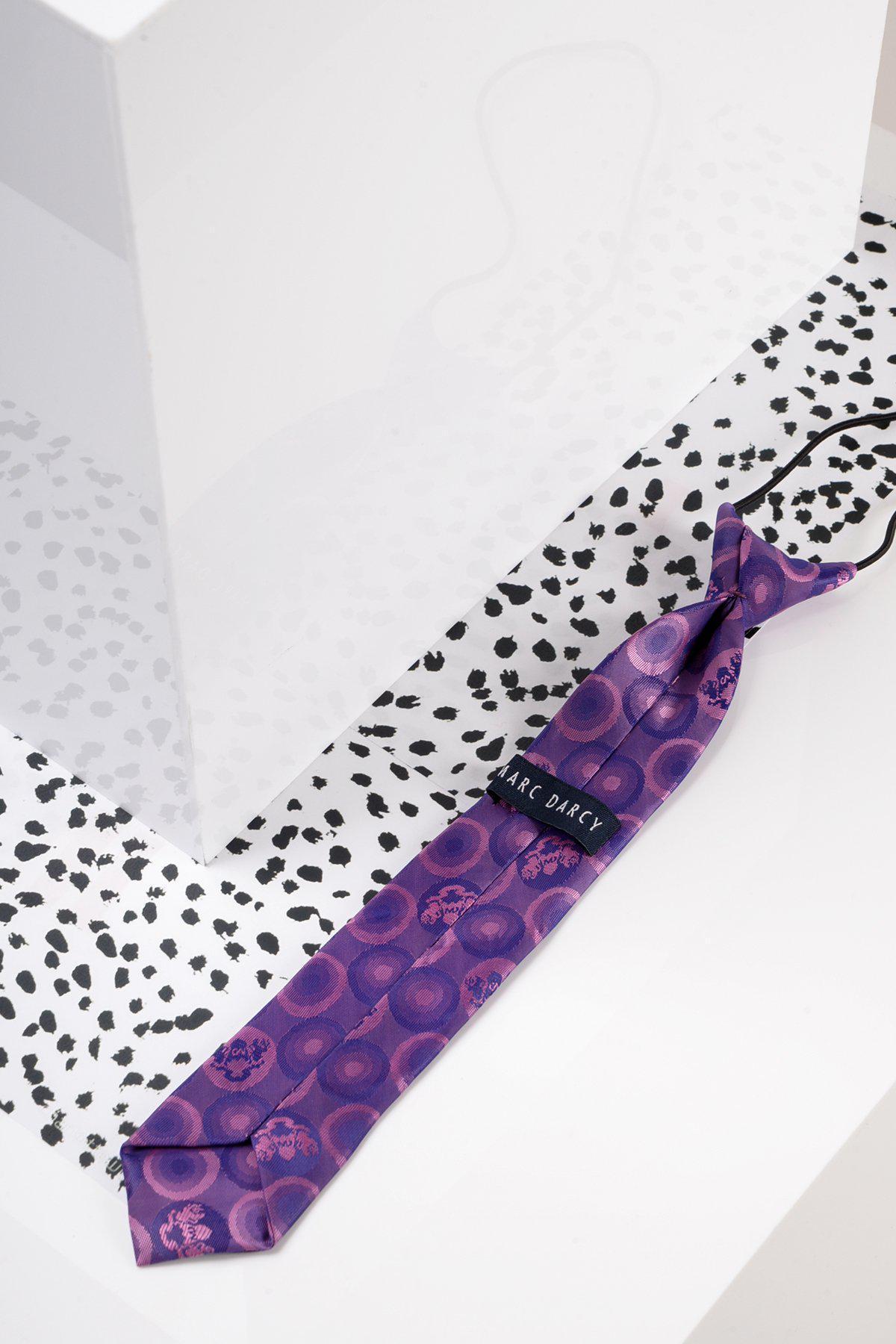 The Marc Darcy Children's Purple Bubble Circle Print Tie rests on a white surface with black spots beside a glossy geometric object—ideal for pairing with boys’ partywear or swapping for an adjustable silk bow tie.