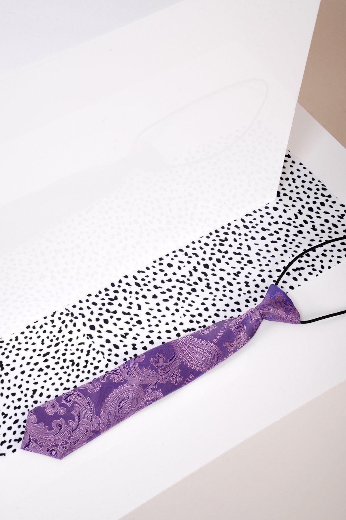 The Marc Darcy Children's Purple Paisley Print Tie with an adjustable neck strap is displayed on a white surface beside black and white speckled paper.