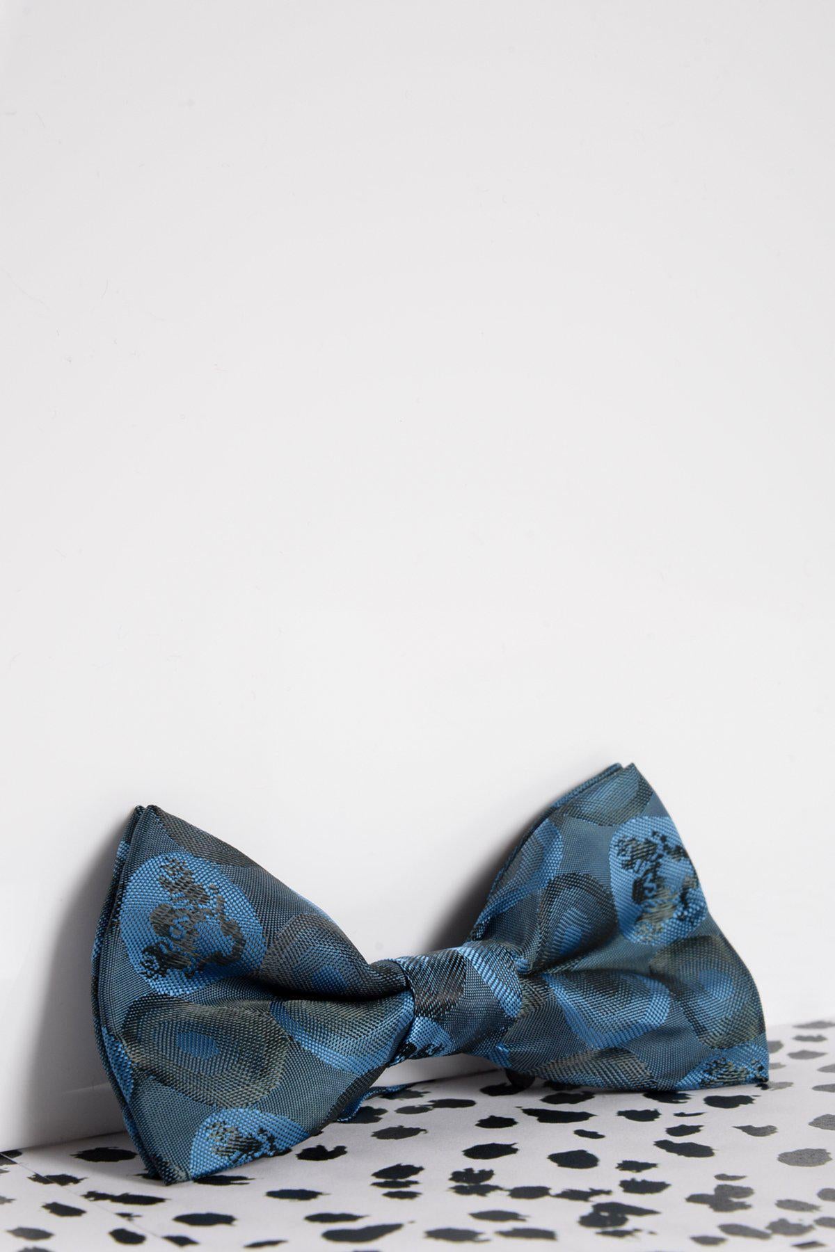The Marc Darcy Childrens Sky Teal Bubble Circle Print Bow Tie is shown on a white background atop a black and white speckled surface—an ideal accessory for special occasions.