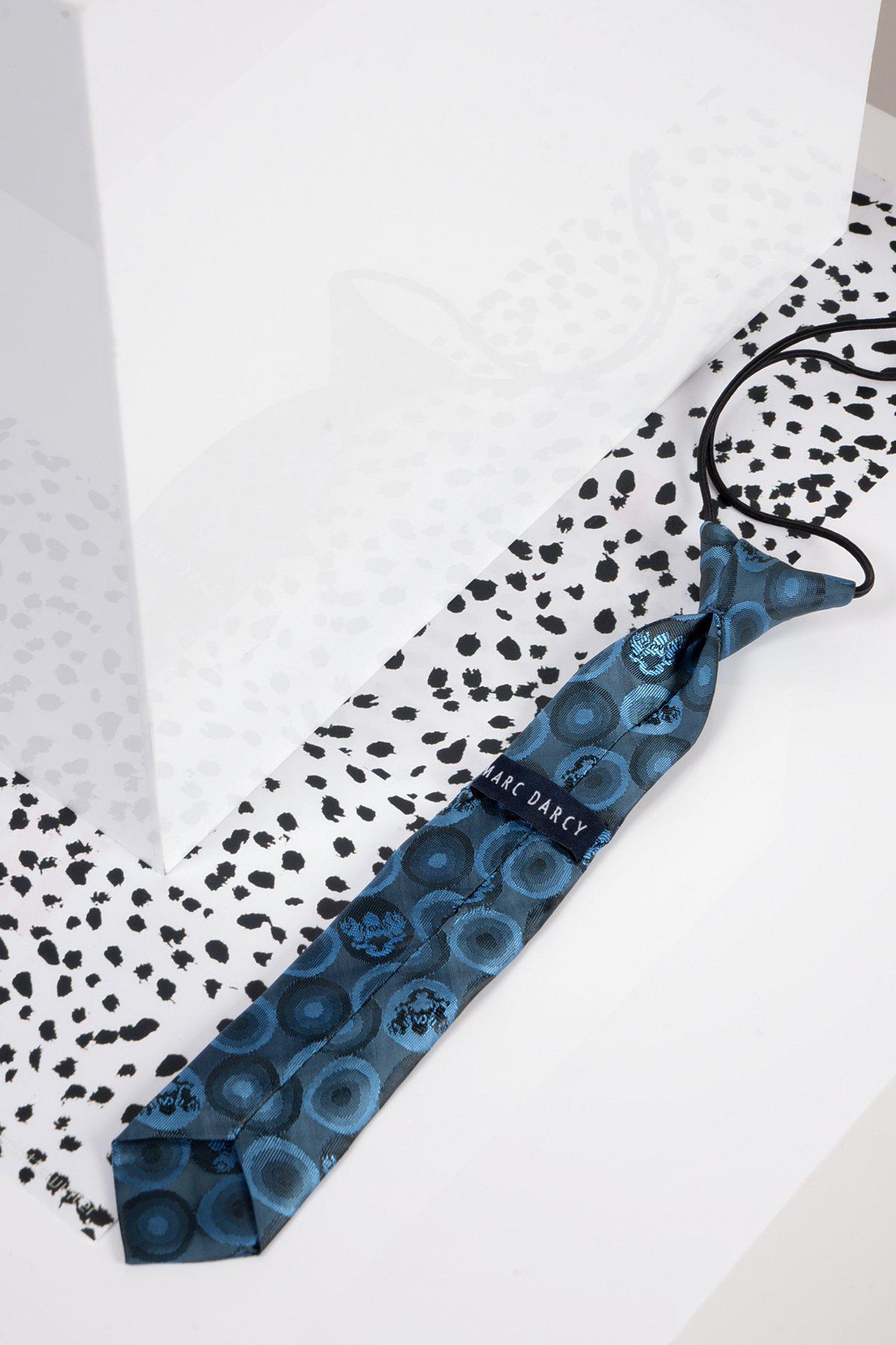 The Children's Sky Teal Bubble Circle Print Tie by Marc Darcy, featuring circular designs and logo print, rests on a white surface with black spots beside a reflective geometric structure.
