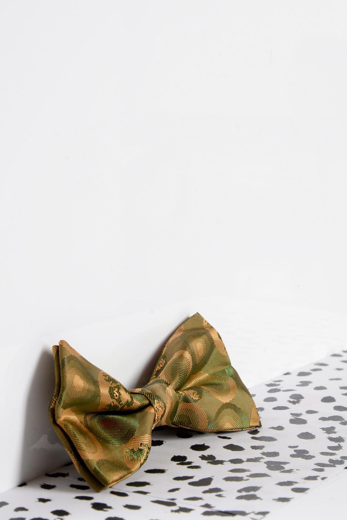 The Marc Darcy Childrens Tan Gold Bubble Circle Print Bow Tie rests against a white wall with a black and white spotted surface in the foreground—an ideal accessory to elevate any childs formal outfit.
