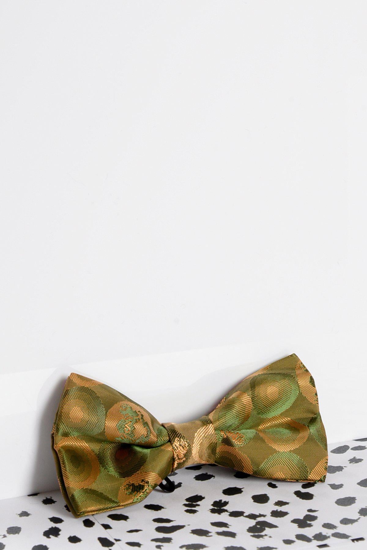 The Marc Darcy Children's Tan Gold Bubble Circle Print Bow Tie sits on a black and white spotted surface with a white background, offering a stylish formal accessory for kids.