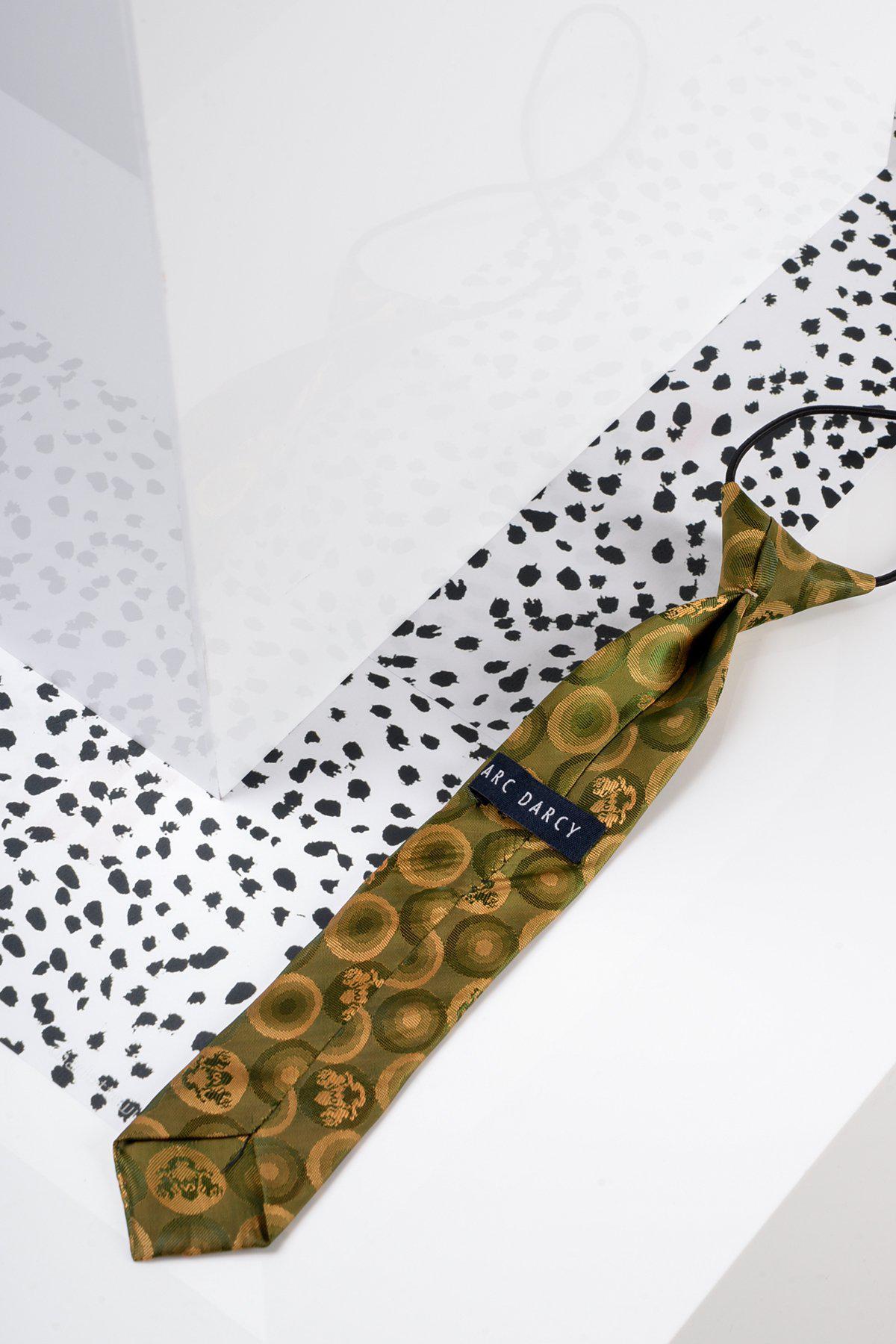 A Marc Darcy Children's Tan Gold Bubble Circle Print Tie rests on a white and black spotted surface, positioned beside clear and white geometric objects.