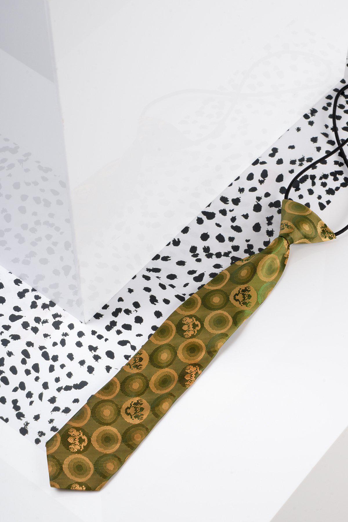 The Marc Darcy Childrens Tan Gold Bubble Circle Print Tie rests on a white surface with black spots beside a glossy white panel—ideal for adding a formal touch to kids three-piece suits.