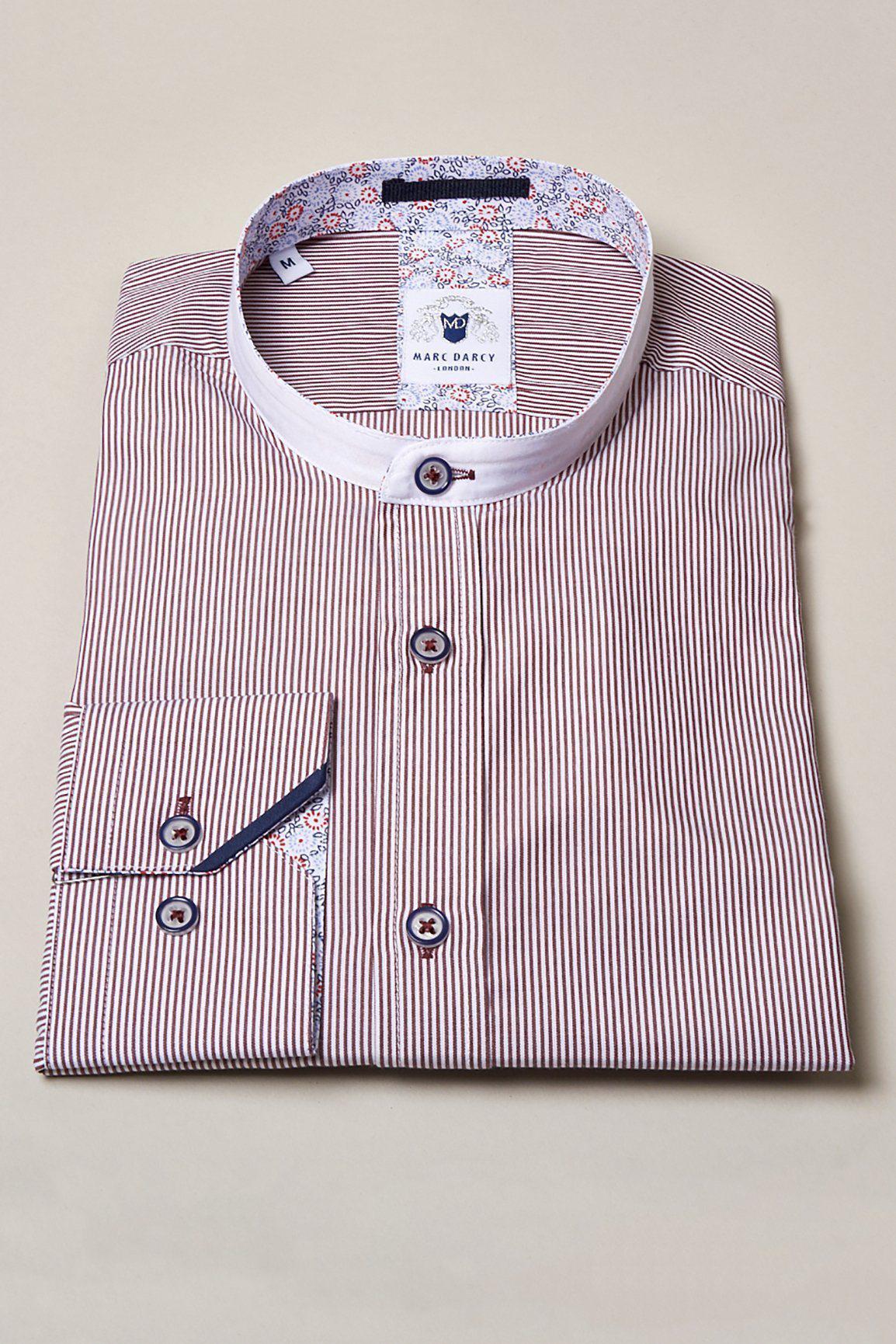 The COOPER - Grandad Collar Wine Stripe Shirt by Marc Darcy features thin red and white stripes, a crisp white collar, contrast buttons, and floral details inside the collar and cuffs. It’s showcased folded on a plain beige background.
