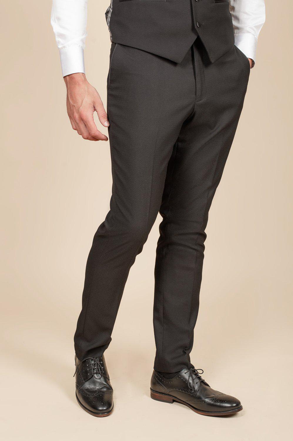 A man models the marcdarcy Dalton Black Tuxedo, as worn by Im A Celebrity Get Me Out Of Here 2022 runner-up Owen Warner—perfect for black-tie events. He poses in slim-fit attire with one hand in his pocket; face is not shown.