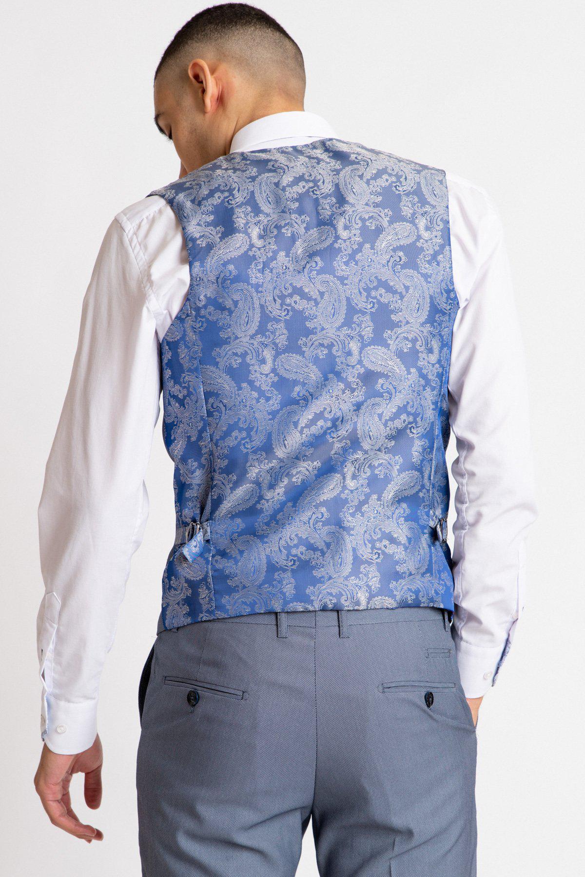 A man wears a white dress shirt, gray dress pants, and the Marc Darcy DANNY Blue Grey Single Breasted Waistcoat, his back to the camera—an elegant take on classic office wear.