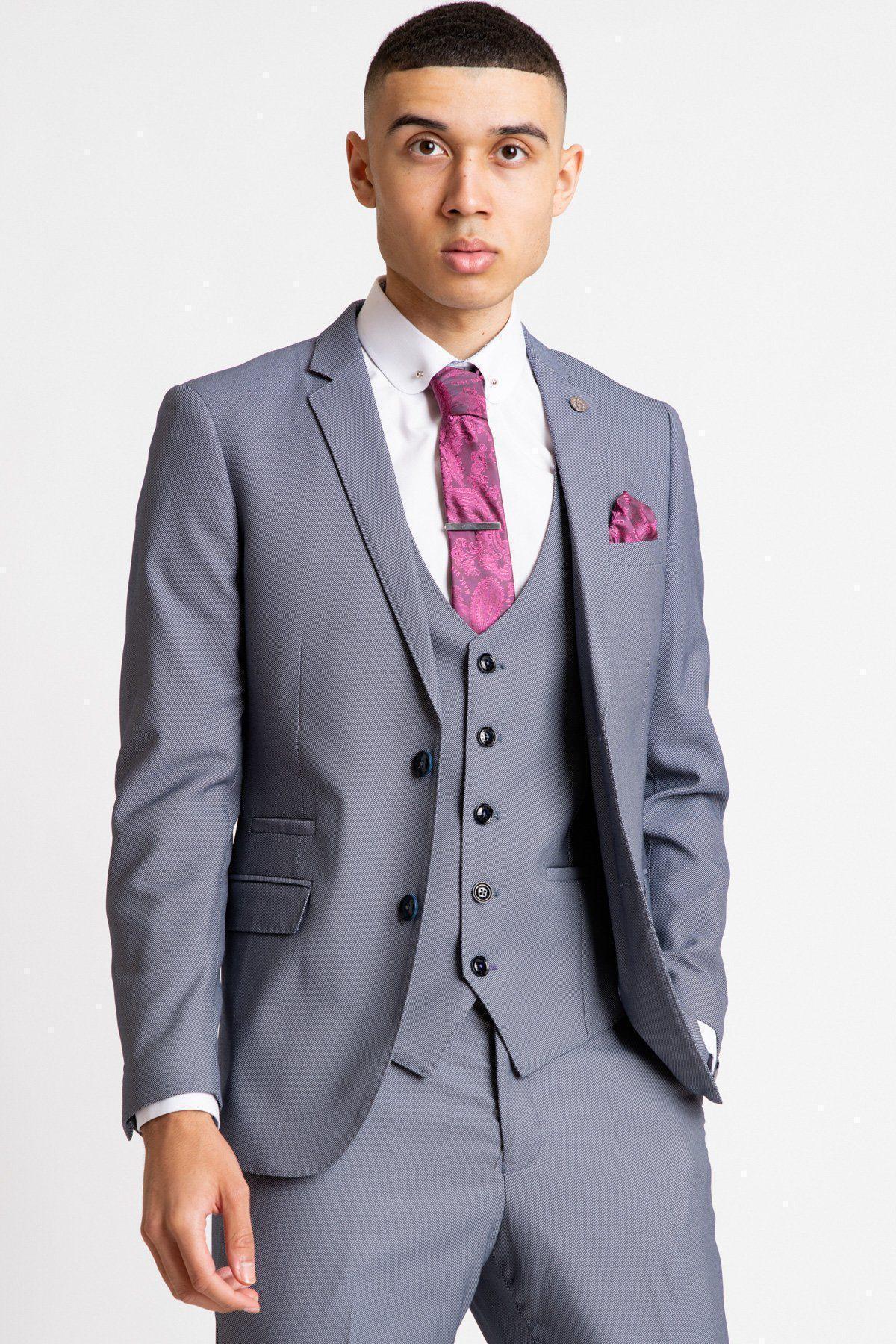 A young man in a light gray three-piece suit with a white shirt, pink patterned tie, and pocket square stands confidently, ready to swap his jacket for the Marc Darcy DANNY - Blue Grey Tailored Blazer, against a plain white background.