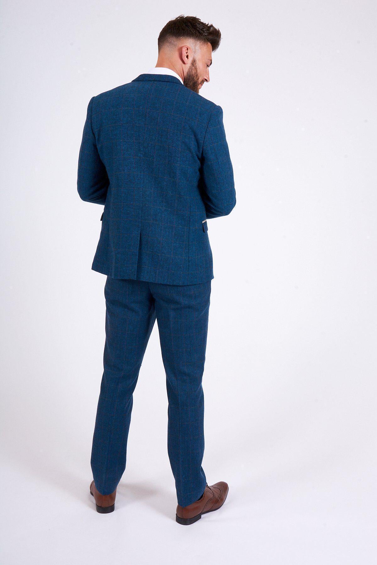 A man faces away, wearing the marcdarcy DION Blue Tweed Check Suit with DX7 Oak Waistcoat and brown shoes. He looks slightly down to his right, set against a plain white background, highlighting refined tailoring.