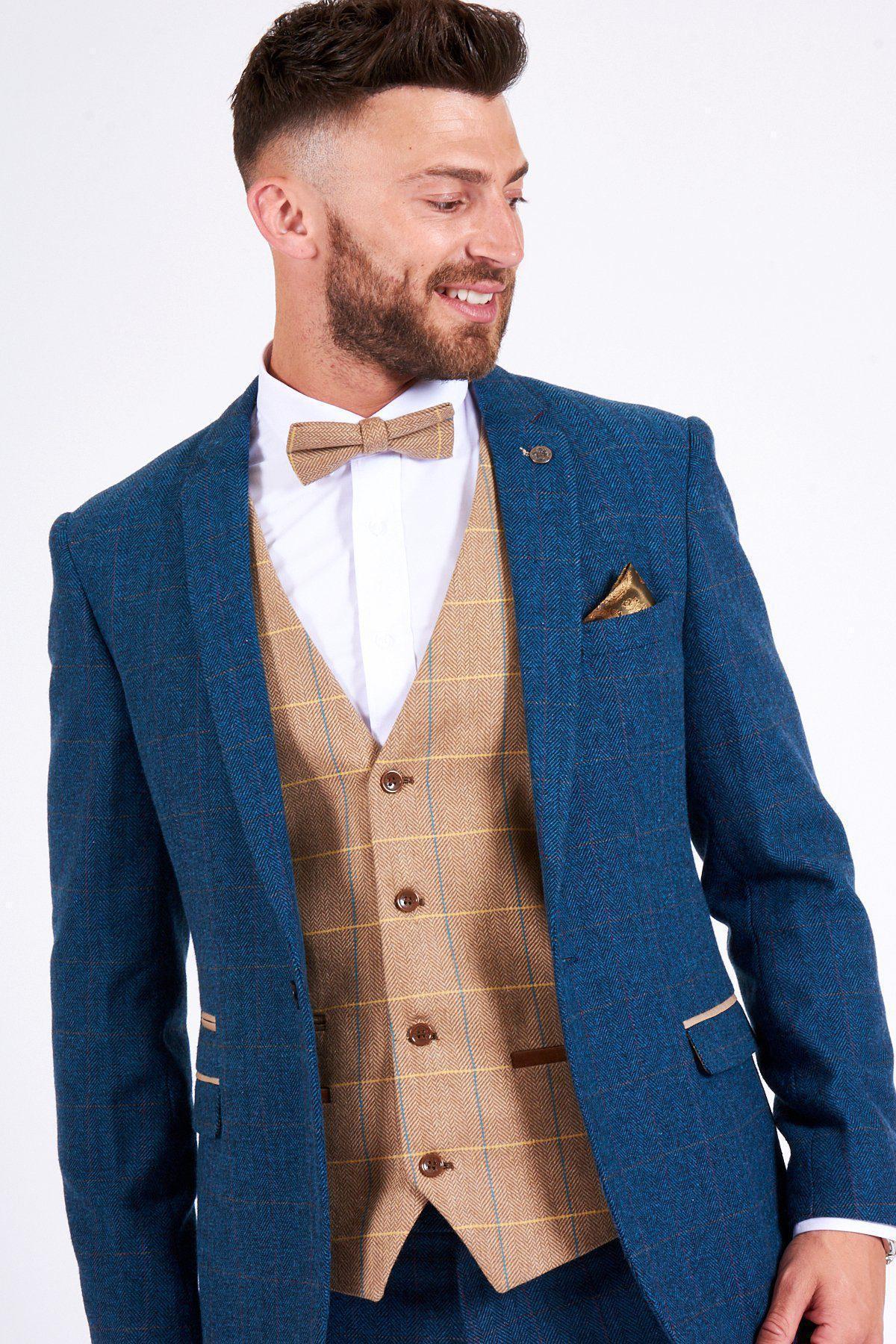 A man smiles, wearing the marcdarcy DION blue tweed check suit with a DX7 Oak waistcoat, white shirt, and tan bow tie. A patterned pocket square accents his wedding look, adding charm and polish.
